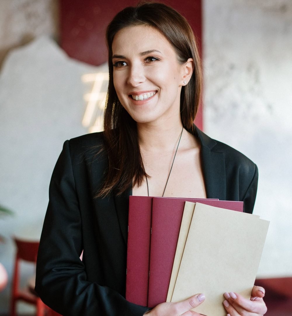 Young woman holding menus, smiling in stylish café interior.